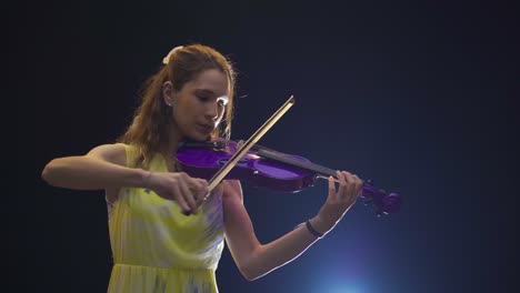 Young-woman-masterfully-plays-the-violin-on-a-dark-stage.